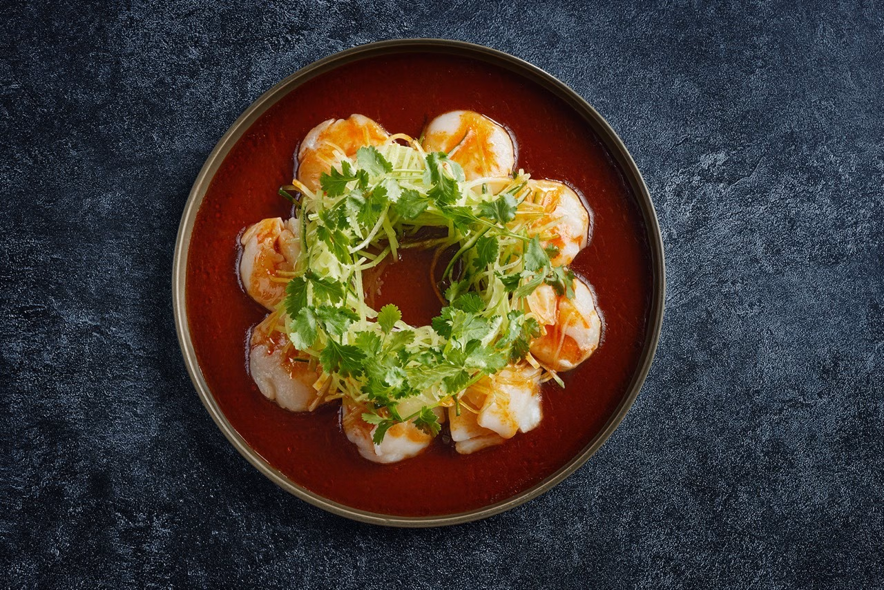 ラー油の周囲にホタテを並べ、緑の香草と細切り具材を添えた料理写真