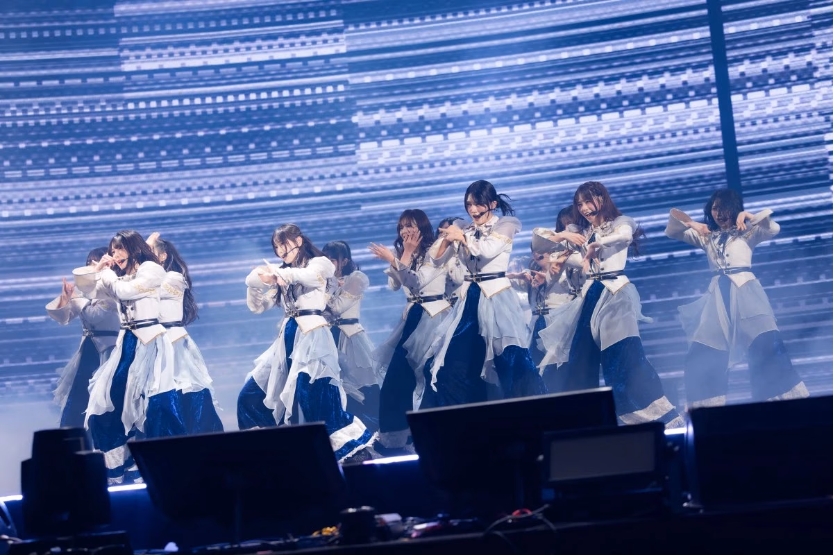Sakurazaka46 perform arm movements in formation in layered white and dark-blue outfits