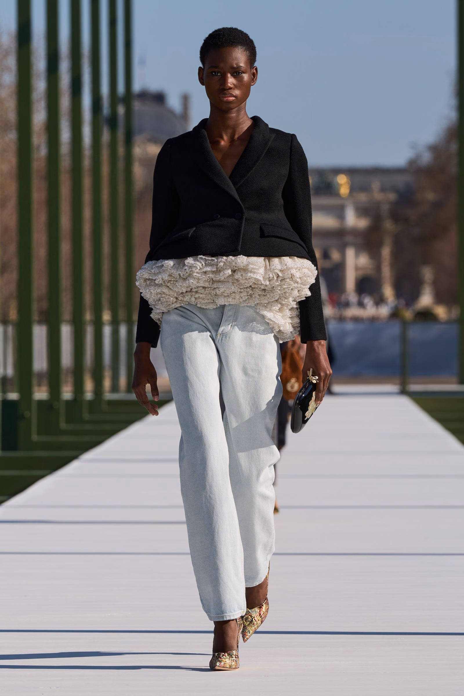A Dior black jacket with pale ruffled layers and light denim trousers