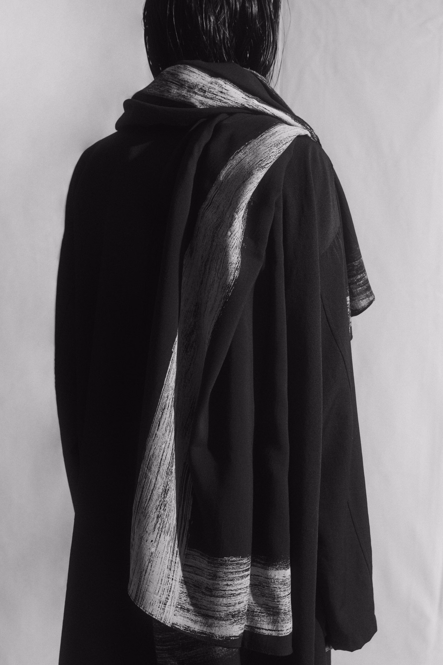 Long scarf with light and dark borders draped down a model’s back