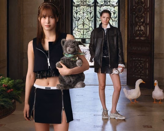 지퍼 크롭 상의와 미니스커트 차림으로 회색 인형을 안은 MOMO, 뒤의 인물과 거위 소품