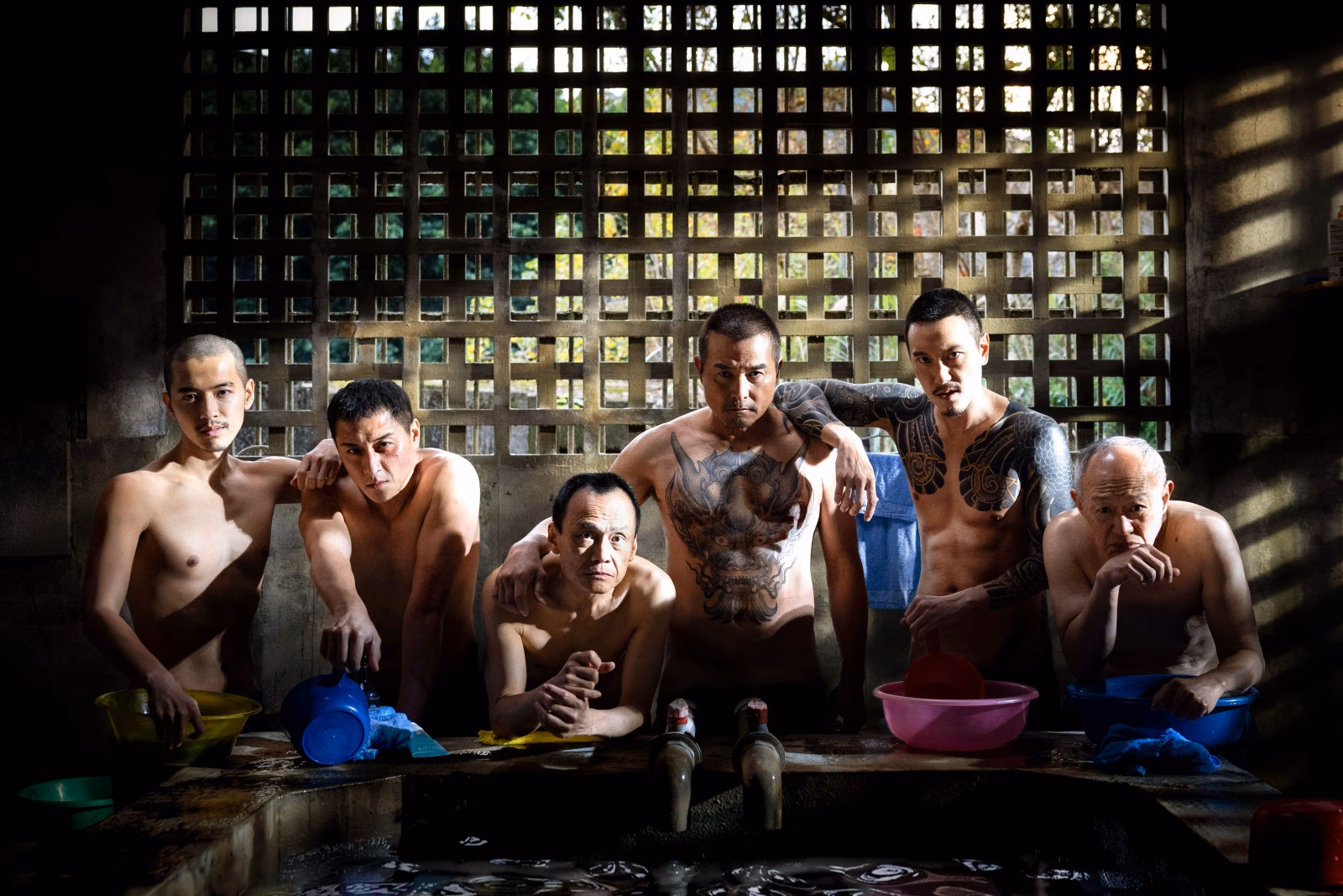 Fictional film still of six characters beside bathhouse basins with a lattice window behind them