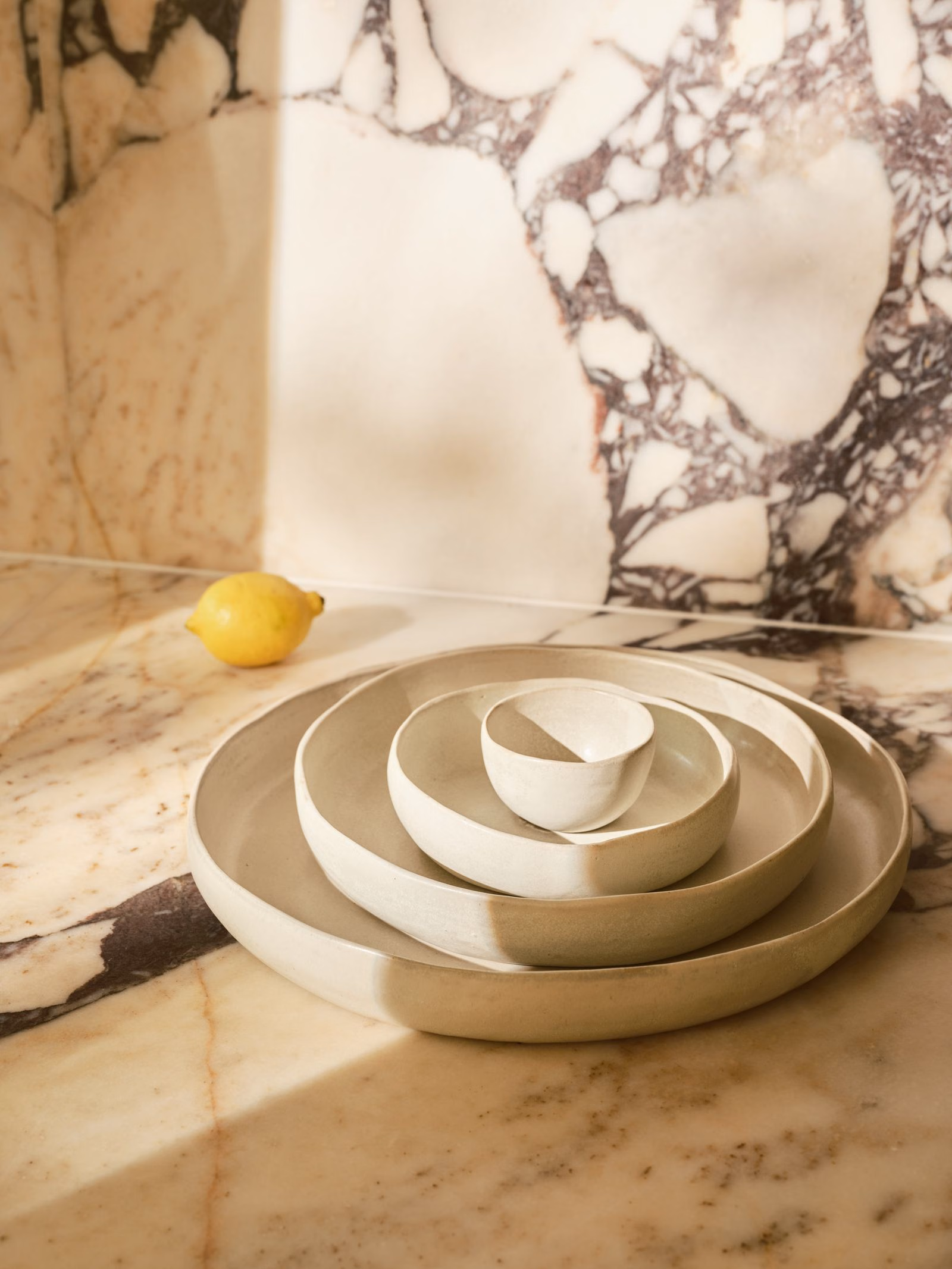 Cream ceramic platters and a bowl with lemons on a stone counter