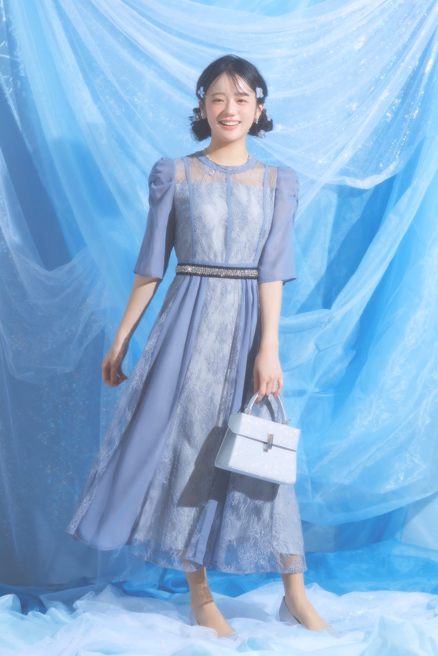 A model in a blue-lilac lace-panel dress with a dark waistband and silver bag