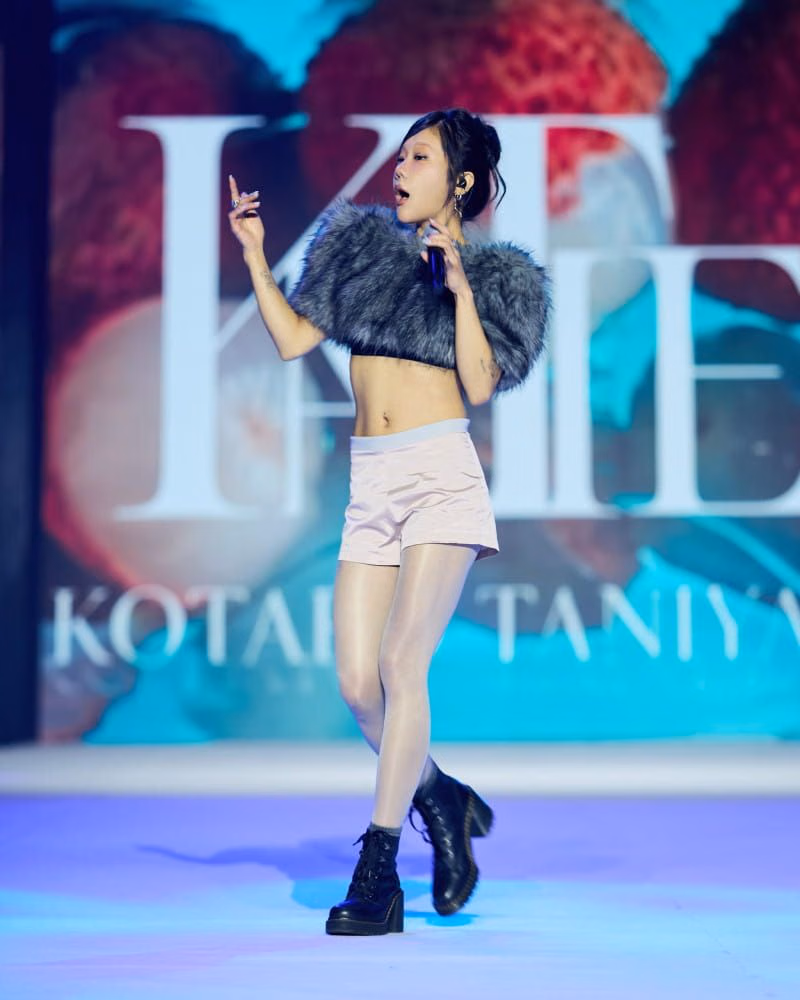 Performer holding a microphone in a grey textured crop top and pale shorts
